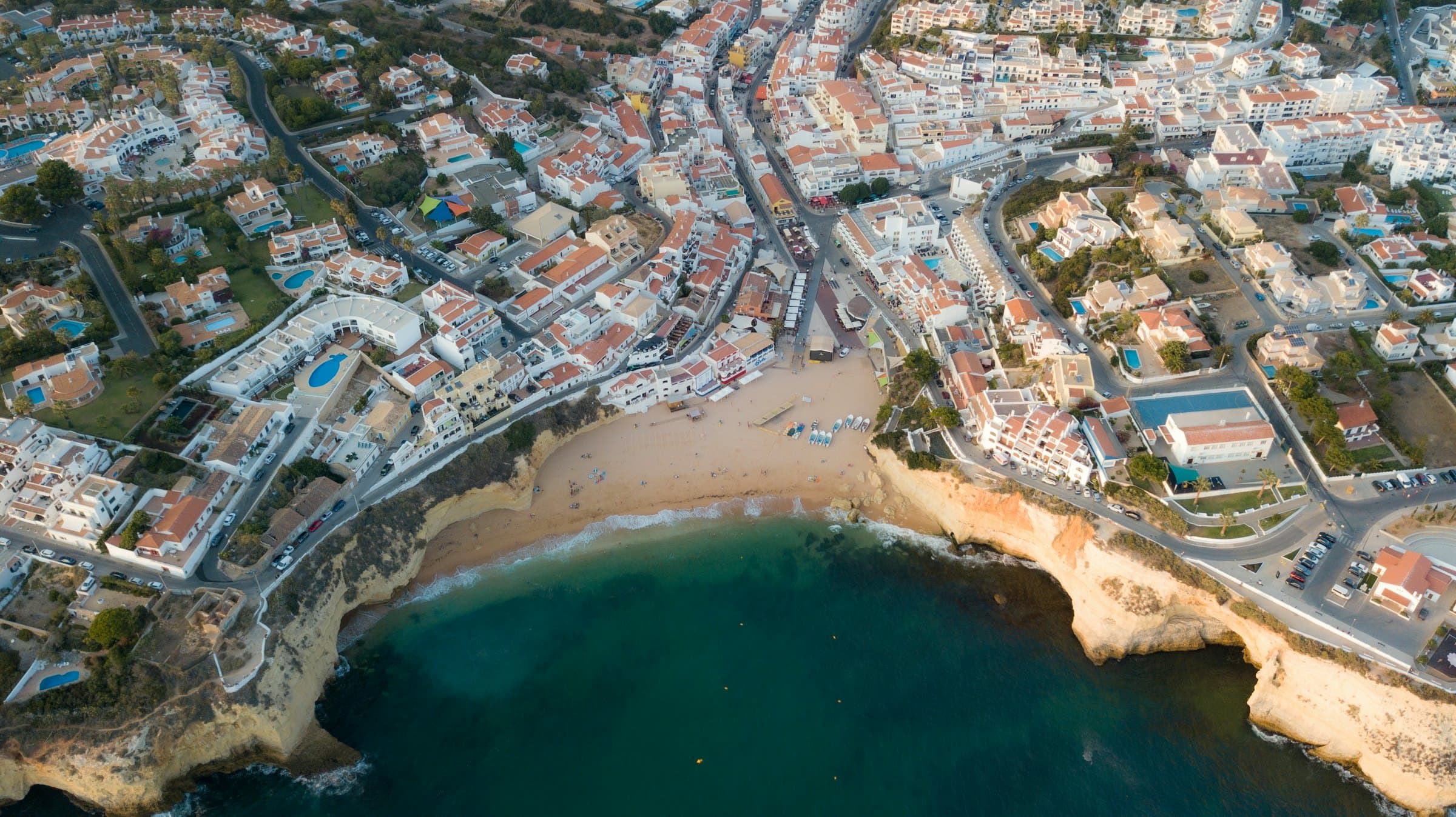 Aerial view of an Algarve coastal town: hundreds of villas, apartments and hotels around a beach between cliffs.