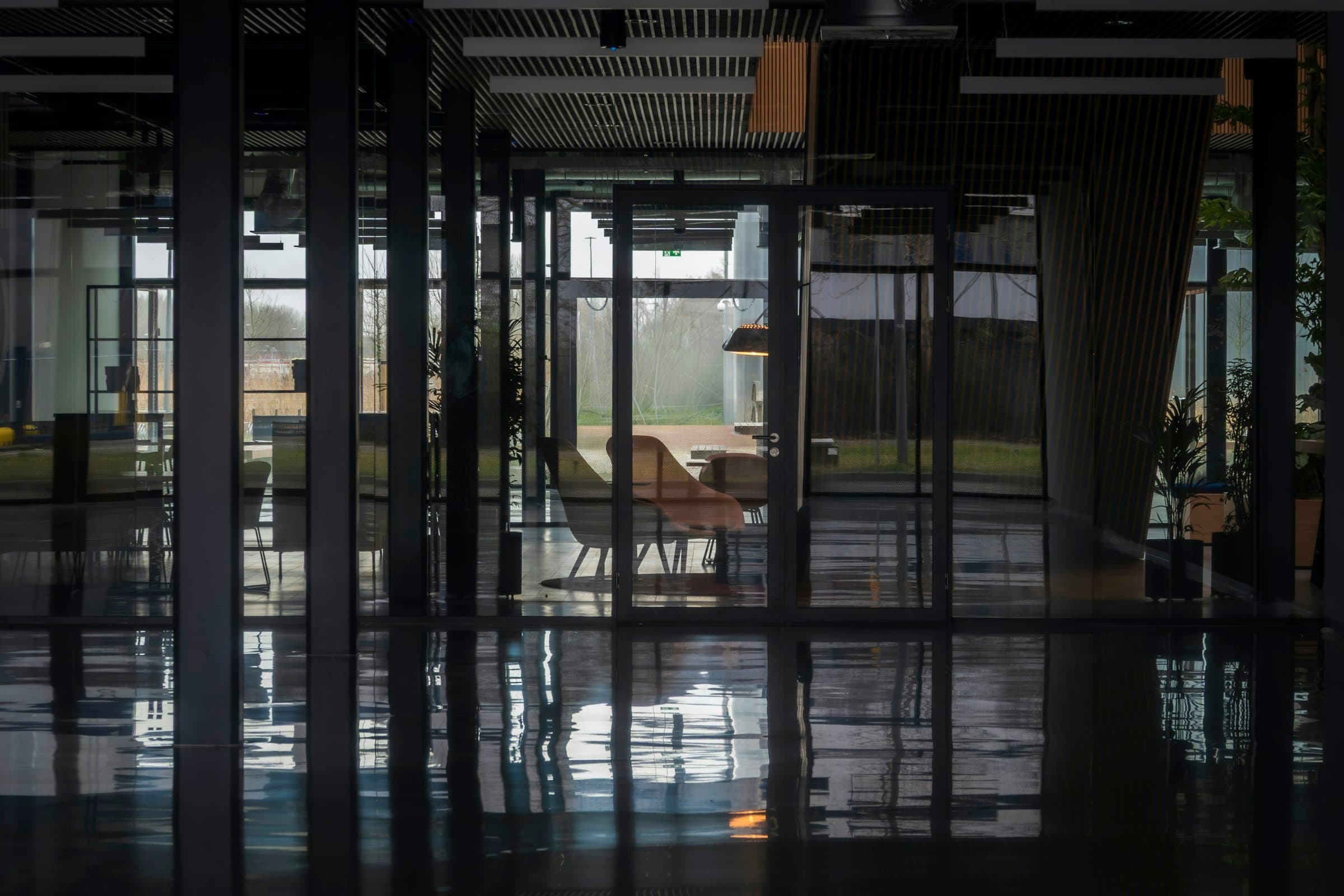 The empty atrium of an office building, glass walls and a polished floor mirroring the light outside.